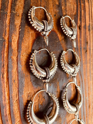 May include: Set of five silver hoop earrings with a decorative design. Each earring has a small, pointed detail hanging from the bottom.